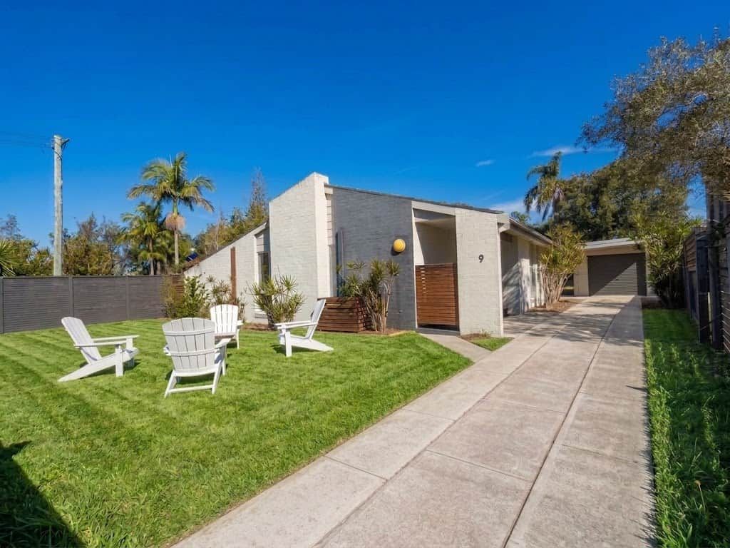 Une maison moderne avec une pelouse bien entretenue et trois chaises Adirondack.