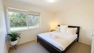 A bedroom with a bed, bedside lamps, a window, and a potted plant.