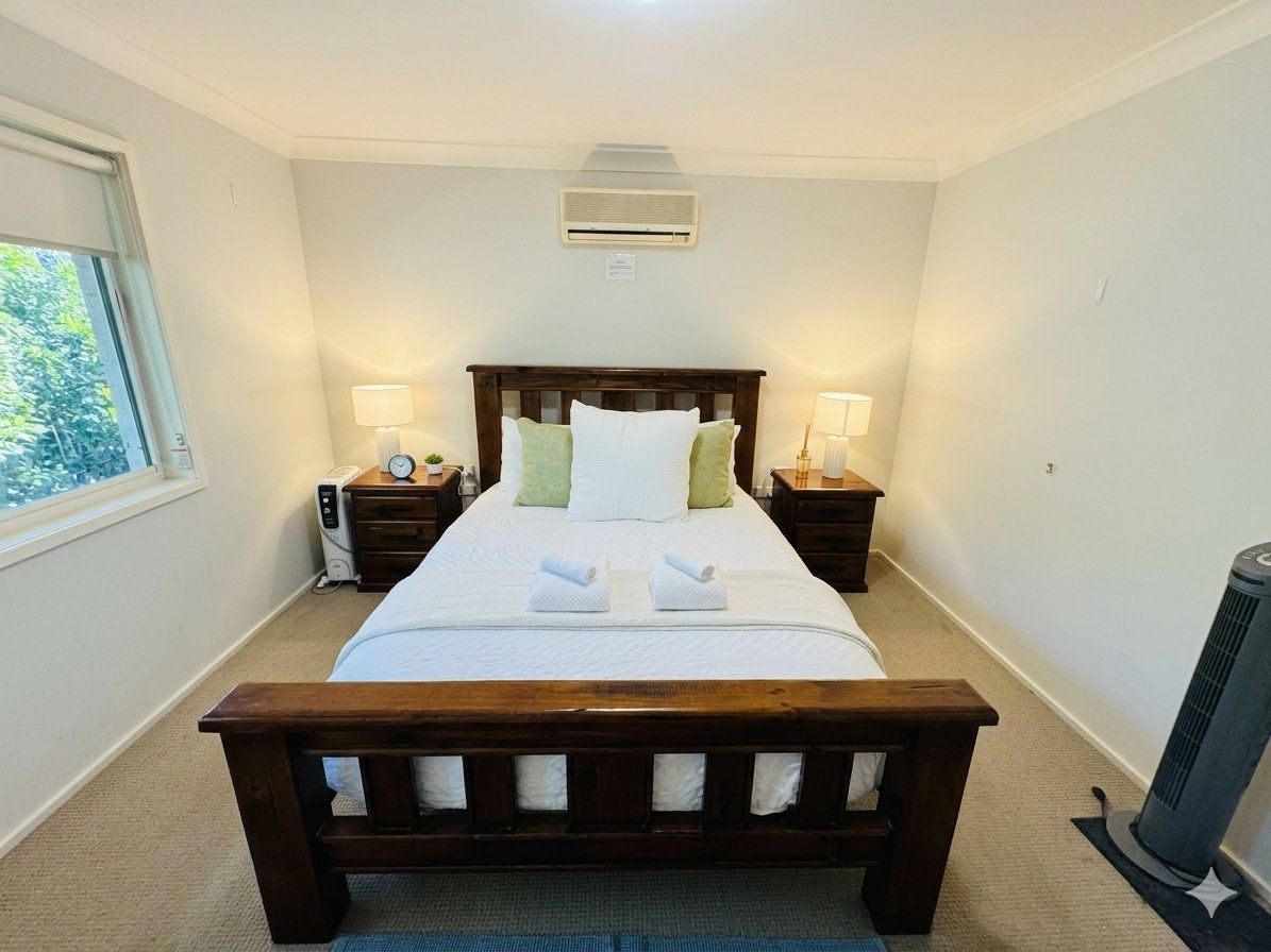 A hotel room with a large bed, bedside tables with lamps, a heater, and a window with a view.