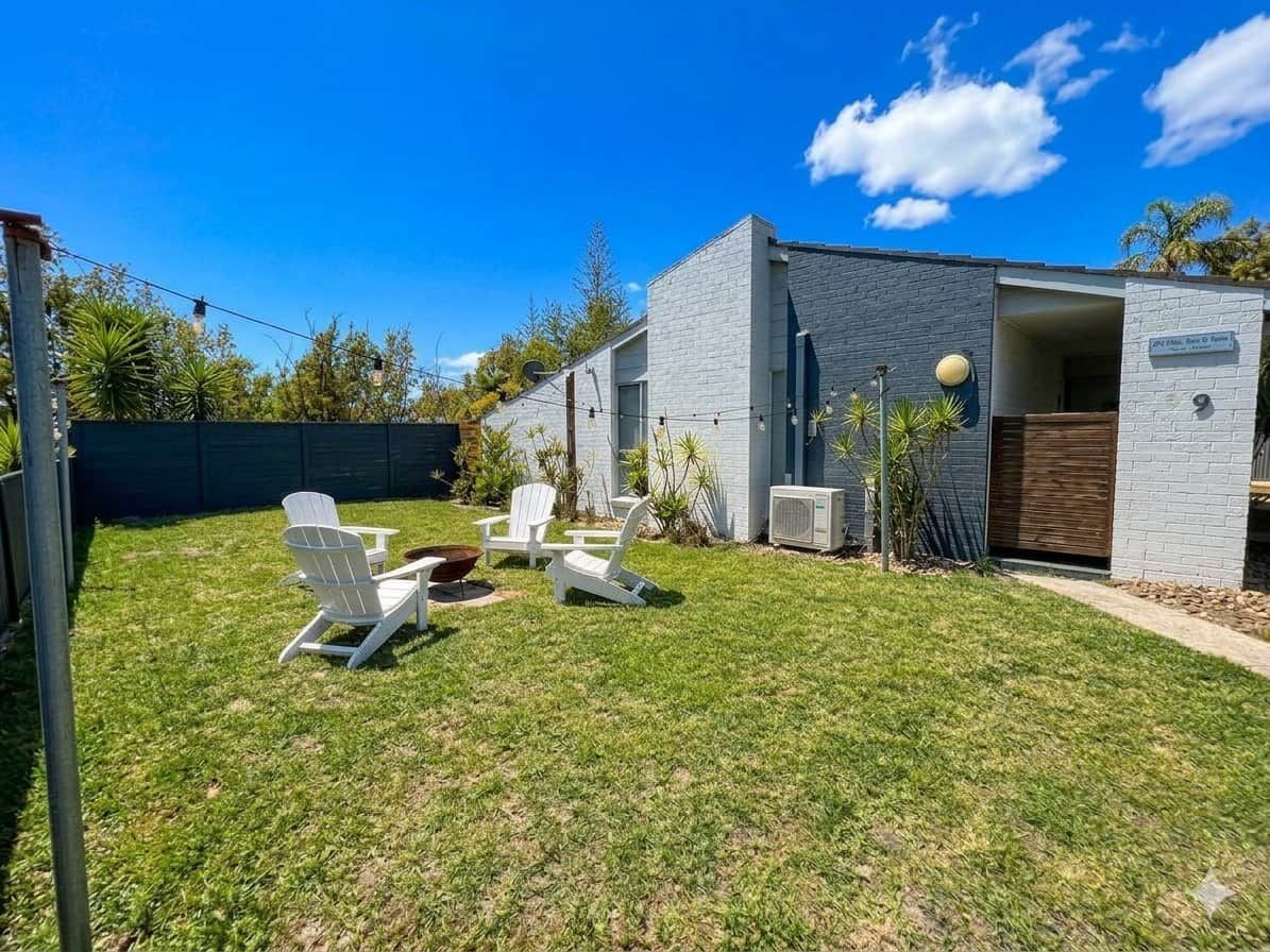 A modern building with a flat roof, a small attached structure, and a well-maintained lawn with outdoor seating.