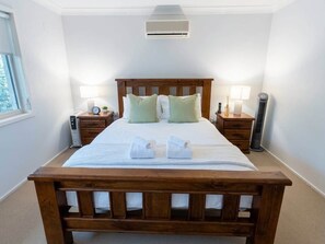 A neatly made bed with a wooden headboard, two bedside tables with lamps, and an air conditioning unit above.