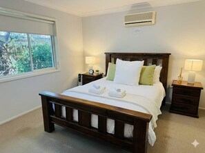Un dormitorio con cama de madera, dos mesitas de noche con lámparas, una ventana y un equipo de aire acondicionado.