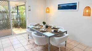 A dining area with a table set for four, chairs, a picture on the wall, and a view through a sliding door. - Samson Sea-clusion 3 bedroom home in Vincentia (Vincentia)