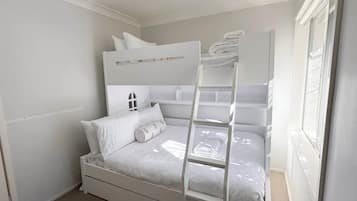 A bunk bed with a ladder, white bedding, and a window with blinds.