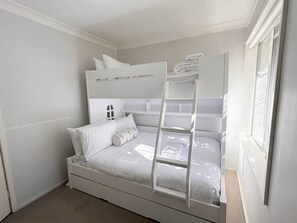 A bunk bed with a ladder, white bedding, and a window with blinds.