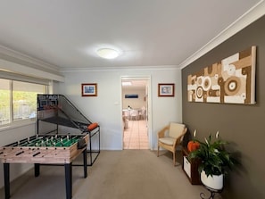 A room with a foosball table, a wall-mounted basketball hoop, a dining area in the background, and a potted plant.