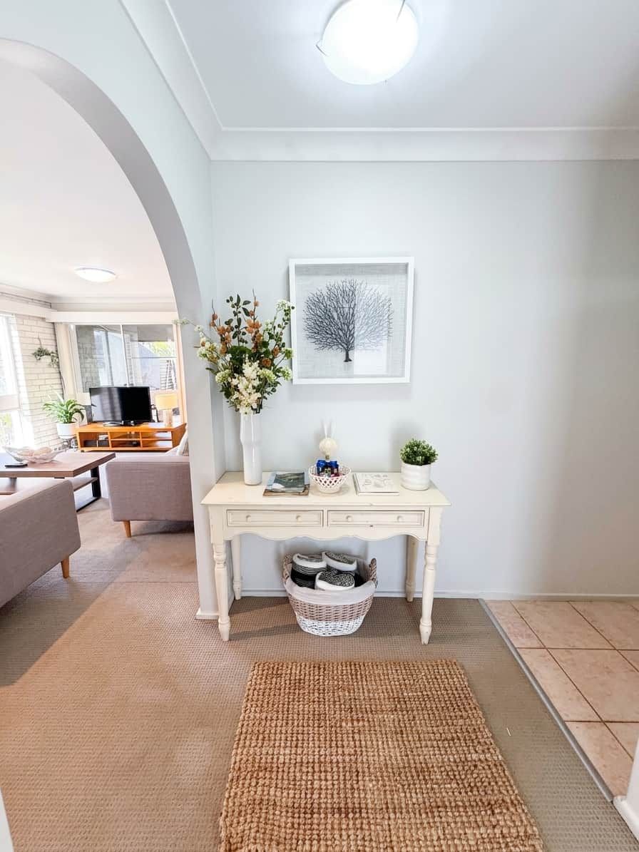 A living room with a white console table, a framed picture, a vase with flowers, a television, and a sofa.