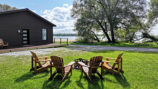 En stuga med en veranda, två Adirondack-stolar och en eldstad.