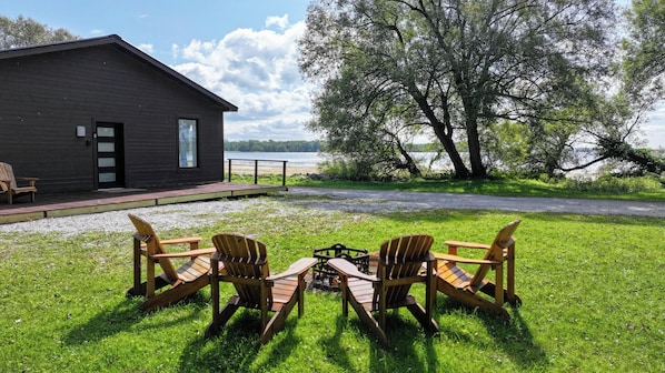 Una cabaña con terraza, dos sillas Adirondack y un pozo de fuego.