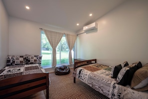 Un dormitorio con dos camas, una ventana con cortinas, un equipo de aire acondicionado y vistas a un paisaje verde.