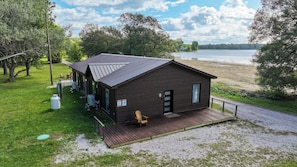 Una cabaña con una terraza, un espacio al aire libre cubierto y vistas a un lago.