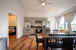Una cocina moderna con armarios grises, un refrigerador de acero inoxidable, un microondas y una estufa. Hay un comedor con una mesa y sillas de madera.