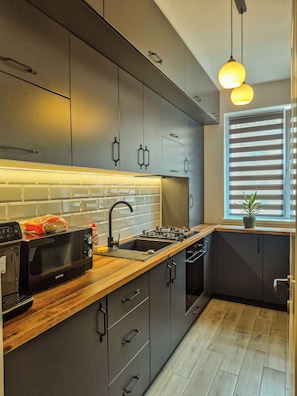 A modern kitchen with dark cabinetry, a wooden countertop, a built-in microwave, and a window with blinds.