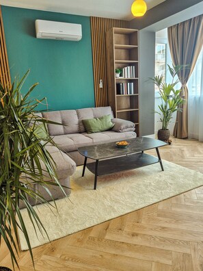 Ein Wohnzimmer mit einer Couch, einem Couchtisch, einem Bücherregal und einer Topfpflanze.