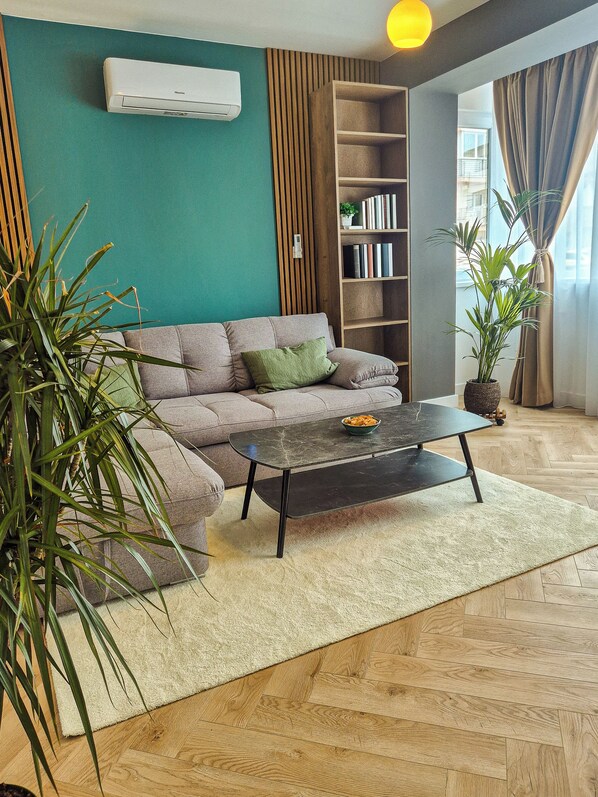 A living room with a sofa, a coffee table, a bookshelf, and a potted plant.