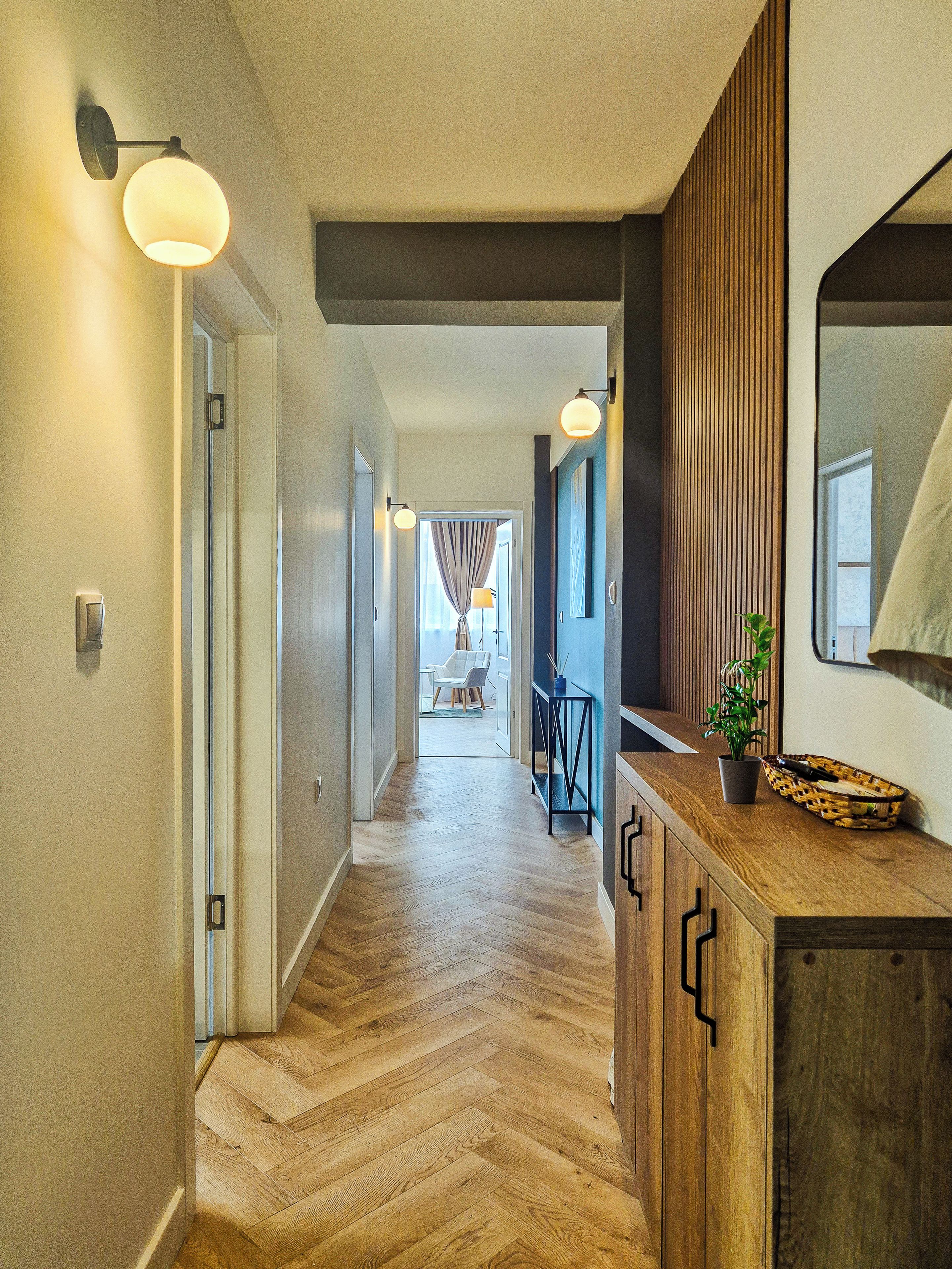 Un couloir doté d’un plancher en bois, d’une armoire en bois avec un miroir et de luminaires fixés au mur.