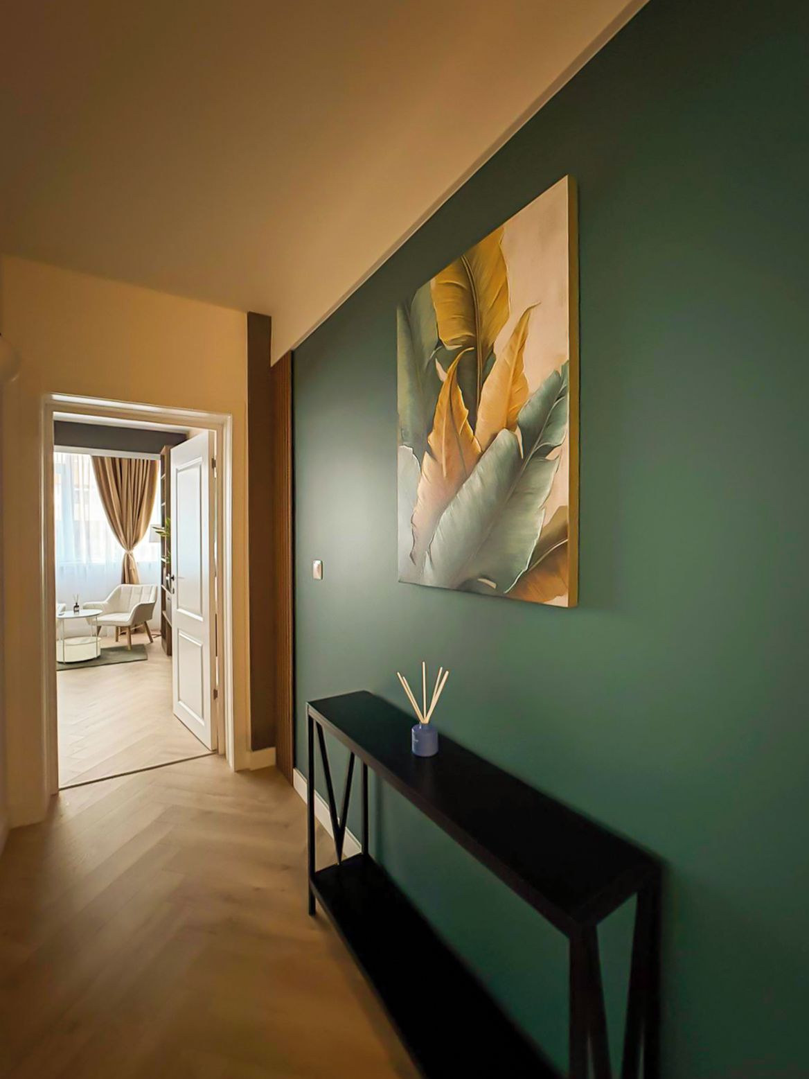 A hallway with a green wall, a black console table, and a door leading to a room with a white chair and a small table.