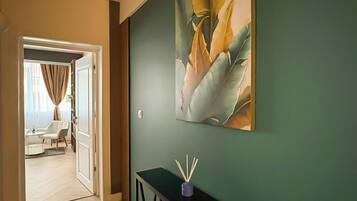 A hallway with a green wall, a black console table, and a door leading to a room with a white chair and a small table.