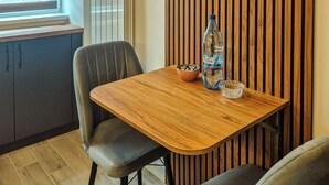 Een modern interieur met een houten wandpaneel, een ronde wandklok, een tafel met stoelen en een raam met zonwering.