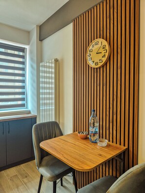 Ein modernes Interieur mit einer Holzvertäfelung, einer runden Wanduhr, einem Tisch mit Stühlen und einem Fenster mit Jalousien.