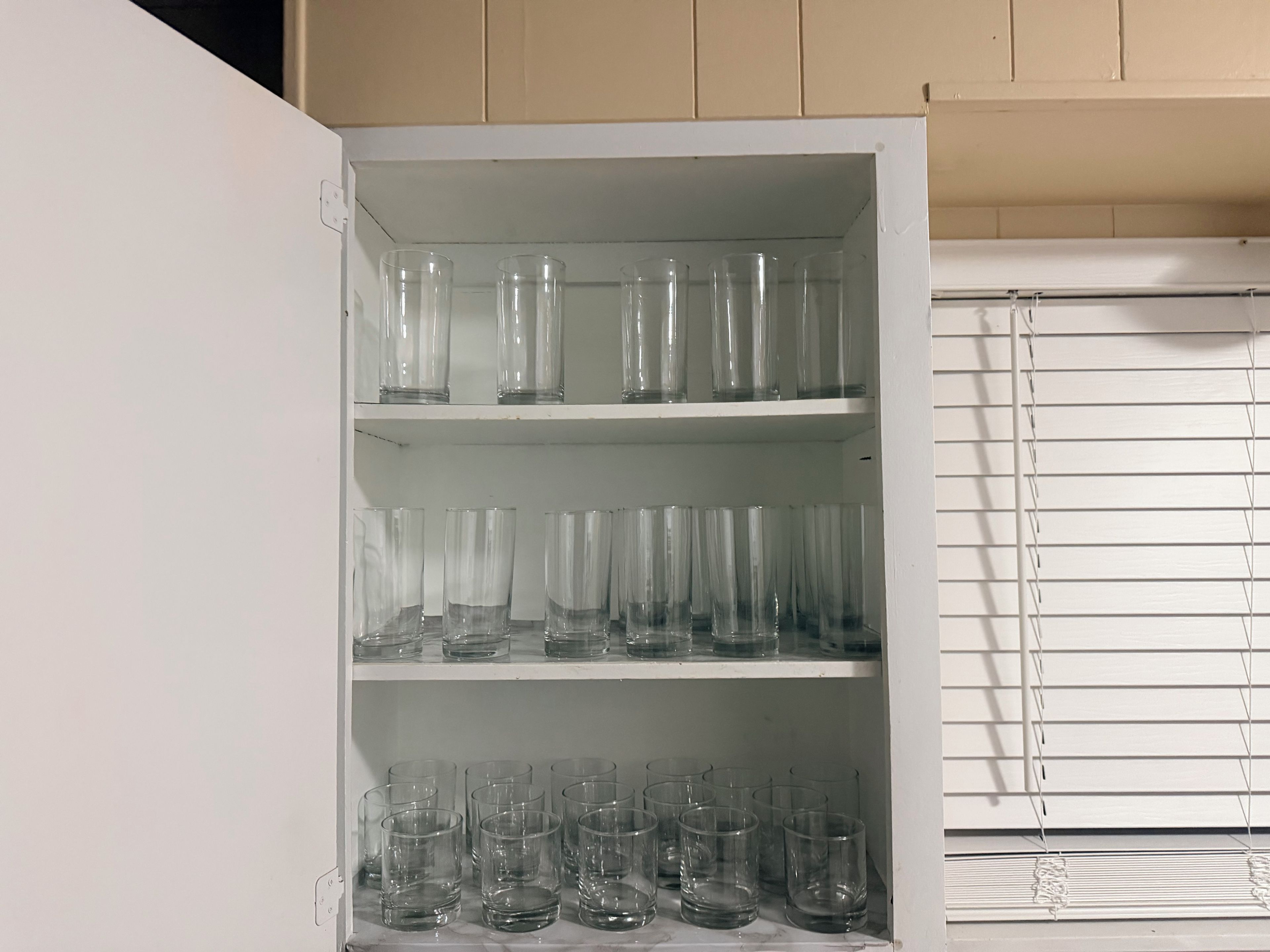 A white cabinet with multiple shelves holding clear glassware.