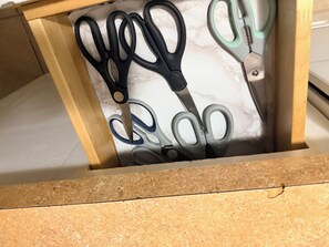 A drawer with a marble-patterned insert containing black and teal scissors.