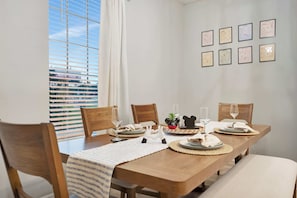A dining area with a wooden table set for four, chairs, a window with blinds, and framed pictures on the wall. - Reunion Village 4BR Mickey and Moana Retreat (Kissimmee)