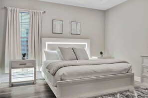 A bedroom with a bed, bedside tables, a nightstand, a window with curtains, and wall art. - Reunion Village 4BR Mickey and Moana Retreat (Kissimmee)