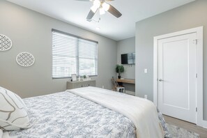 Un dormitorio con cama, ventilador de techo, ventana con persianas, televisor en la pared y una puerta.