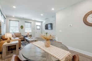Una sala de estar moderna con una mesa de comedor, sofá y televisor montado en la pared.