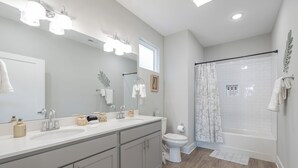 Un bagno moderno con lavabo doppio, servizi igienici, doccia con porta in vetro e un grande specchio con illuminazione a soffitto.