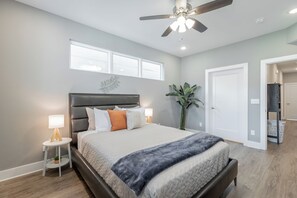 Ein Schlafzimmer mit einem Bett, Nachttischlampen, einem Deckenventilator und einem großen Fenster.