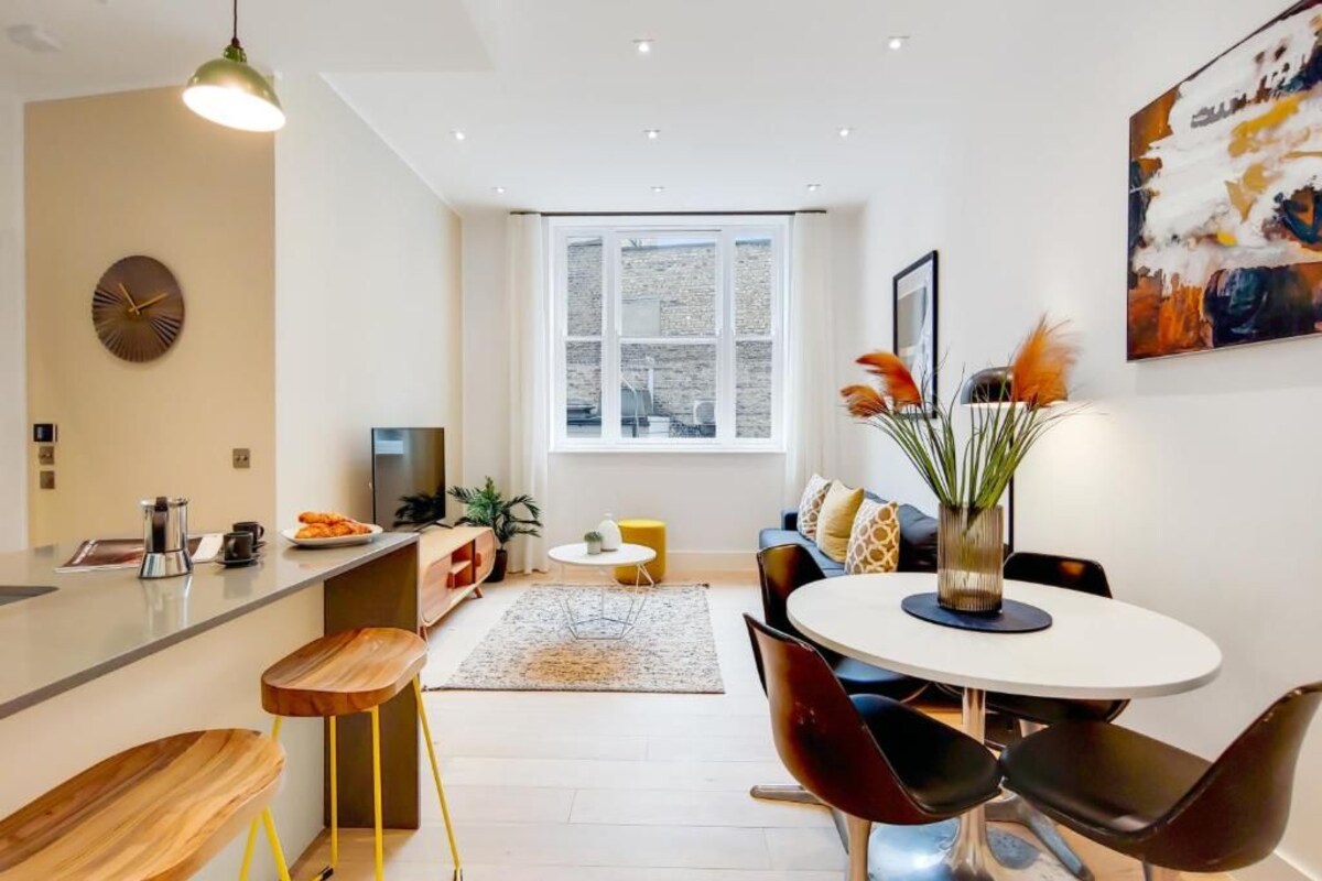 A modern kitchen with a dining area, a large window, and a painting on the wall.