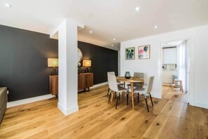 A modern dining area with a round table, chairs, and a dark accent wall. - Spacious Apartments in Borough London Bridge by Short Stories London (London)