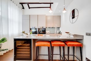 A modern kitchen with a central island, bar stools, and pendant lighting. - Spacious Apartments in Borough London Bridge by Short Stories London (London)
