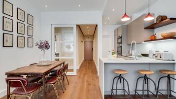 A modern kitchen with a wooden dining table and bar stools, a kitchen island with a sink and a toaster, and framed pictures on the wall.