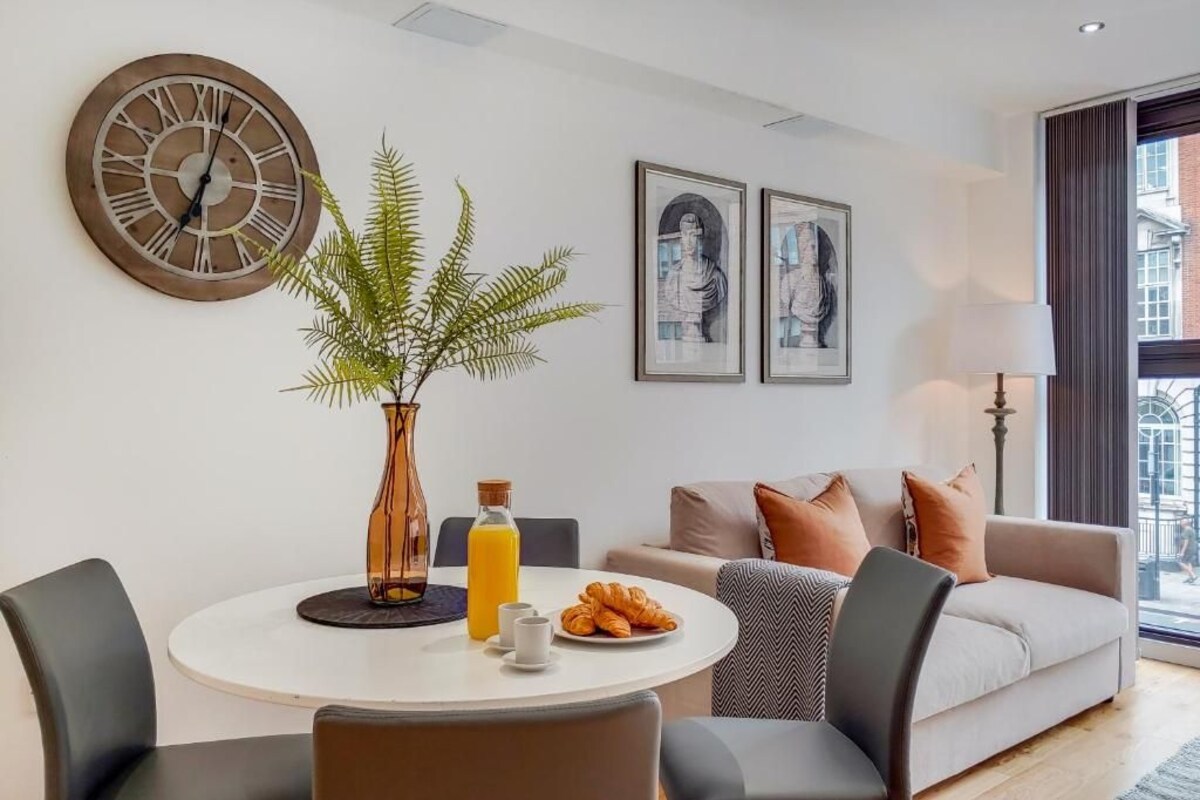 A modern living room with a round dining table, a potted plant, and a sofa with cushions.