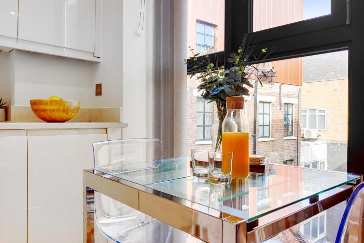 A modern kitchen with a glass table, a bowl, and a vase with plants.