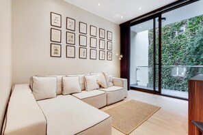 A modern living room with a sectional sofa, a large window with a view of greenery, and framed artwork on the wall. - Spacious Apartments in Borough London Bridge by Short Stories London (London)