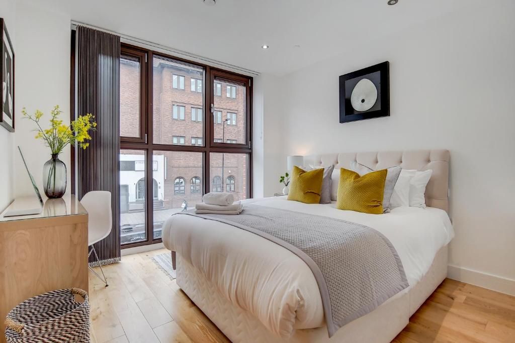 A modern bedroom with a large bed, a desk, and a window with a view of buildings.