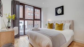 A modern bedroom with a large bed, a desk, and a window with a view of buildings.