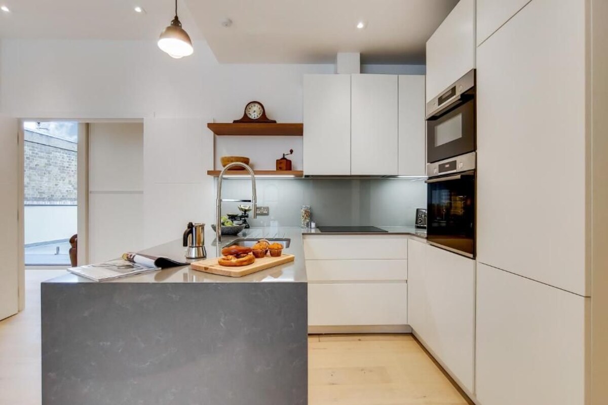 A modern kitchen with white cabinets, a built-in oven, and a wooden countertop with a cutting board and utensils.