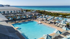 Zwembadcomplex van een resort met meerdere ligbedden en parasols, een centraal gelegen zwembad en uitzicht op de oceaan.