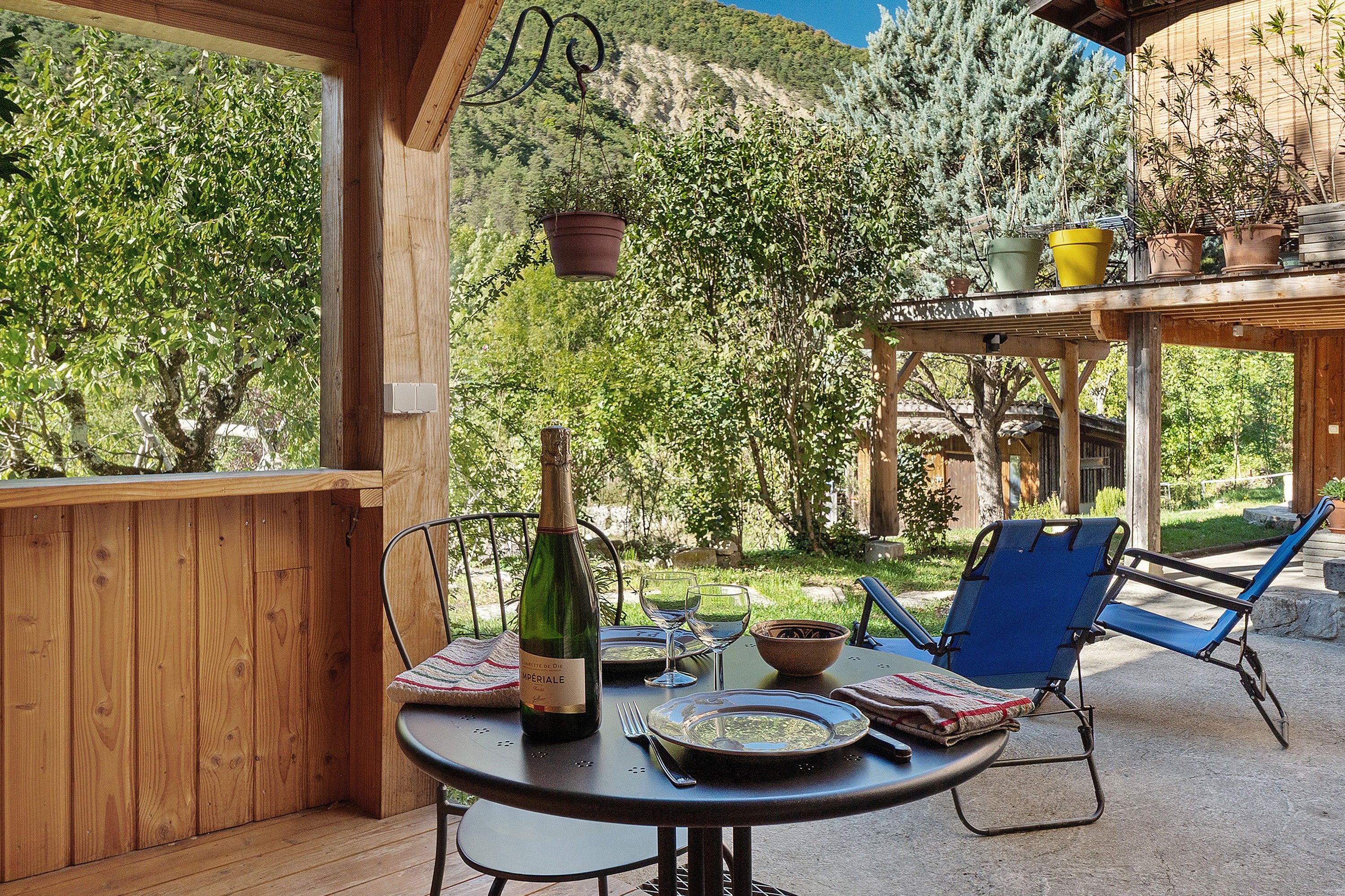 Un espace de restauration en plein air avec une table dressée pour deux personnes, une bouteille de vin et une chaise.