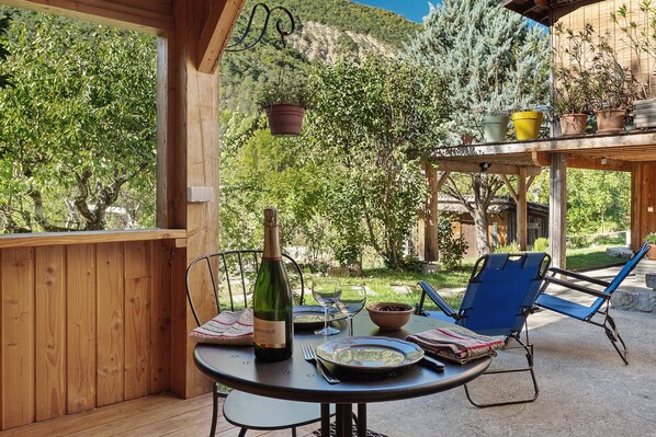 An outdoor dining area with a table set for two, a bottle of wine, and a chair.