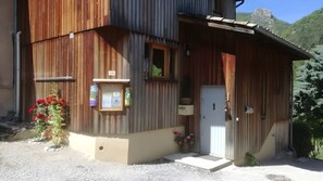 A wooden building with a door, windows, and a small porch area. - Les Baladins Guest House: Mountain View, Private Terrace, Wi-Fi, Open Year-Round (Romeyer)