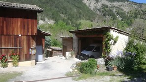 A rustic building with a car parked in front, surrounded by greenery and a mountainous backdrop. - Les Baladins Guest House: Mountain View, Private Terrace, Wi-Fi, Open Year-Round (Romeyer)