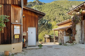 A rustic wooden building with a white door, a gravel path, and a mountainous backdrop.
