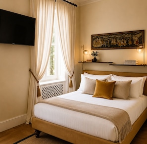 A hotel room with a bed, curtains, a painting, a shelf with books, and a television mounted on the wall. - Casa Rubinacci (Napoli)