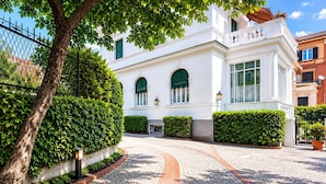 A white building with arched windows and a cobblestone pathway leading to it. - Casa Rubinacci (Napoli)